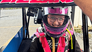 Lizzy Vogel in her racing car wearing a pink helmet and smiling